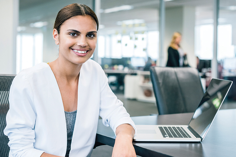 Young indigenous Australian woman seated at meeting room table by laptop.