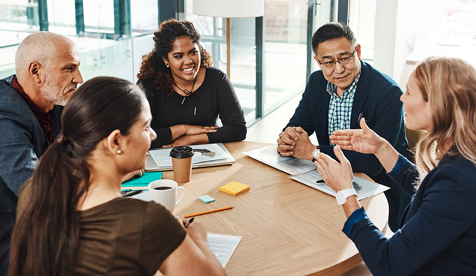 Group of people sitting around a table listening to one woman talk