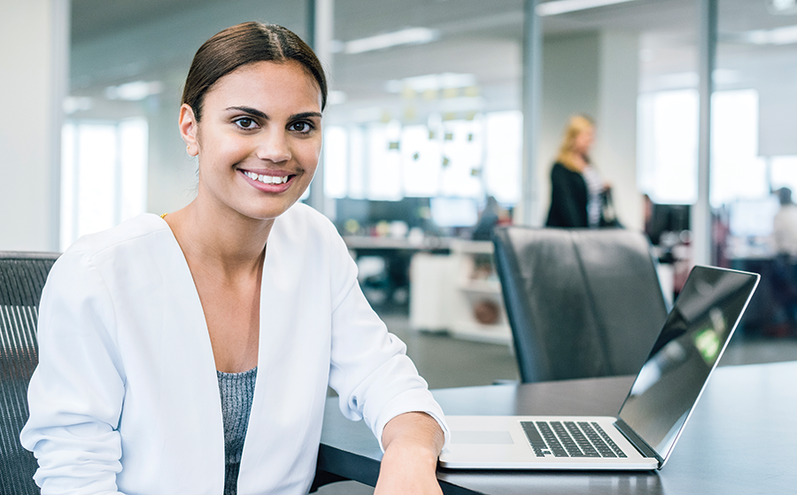 Young woman sitting at a conference table, smiling at the camera with a laptop in front of her
