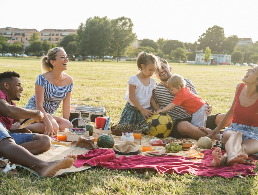 Group of parents enjoy a picnic lunch. Children are playing with a ball with their dad.